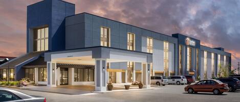 A modern hotel with a covered entrance, multiple parking spaces, and a clear sky.