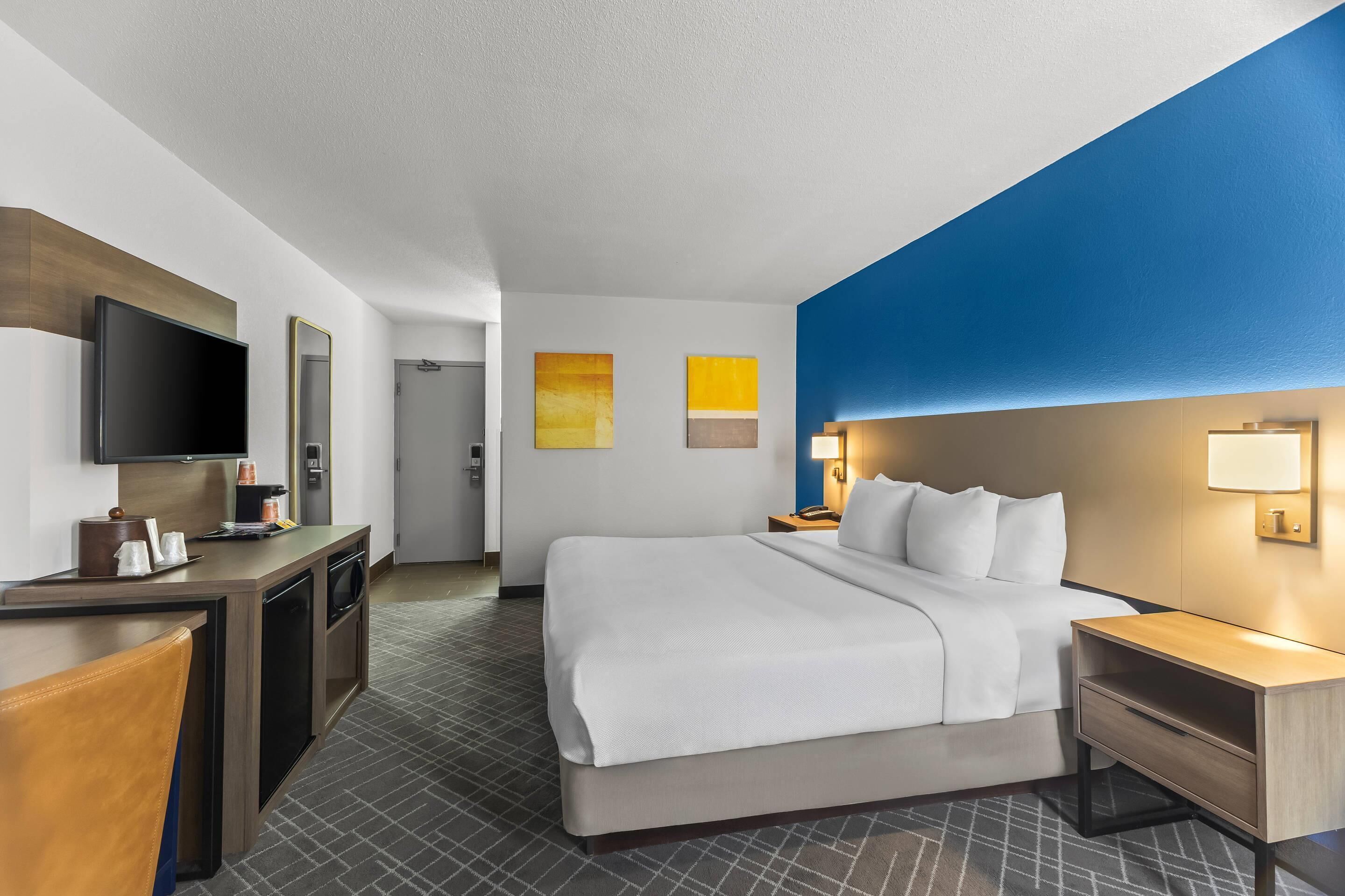Ein Hotelzimmer mit Bett, Nachttischen, Fernseher, Schreibtisch mit Spiegel und Bildern an den Wänden.