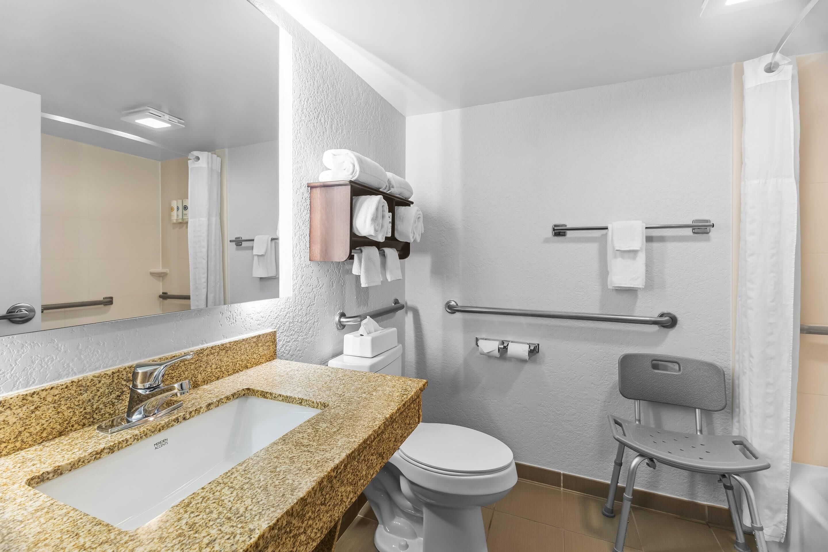 A modern bathroom with a granite countertop sink, a white toilet, a shower with a glass door, and a grab bar for safety.