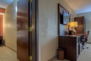 Ein Hotelzimmer mit Holztür, Schreibtisch mit Lampe, Stuhl und Mülleimer.