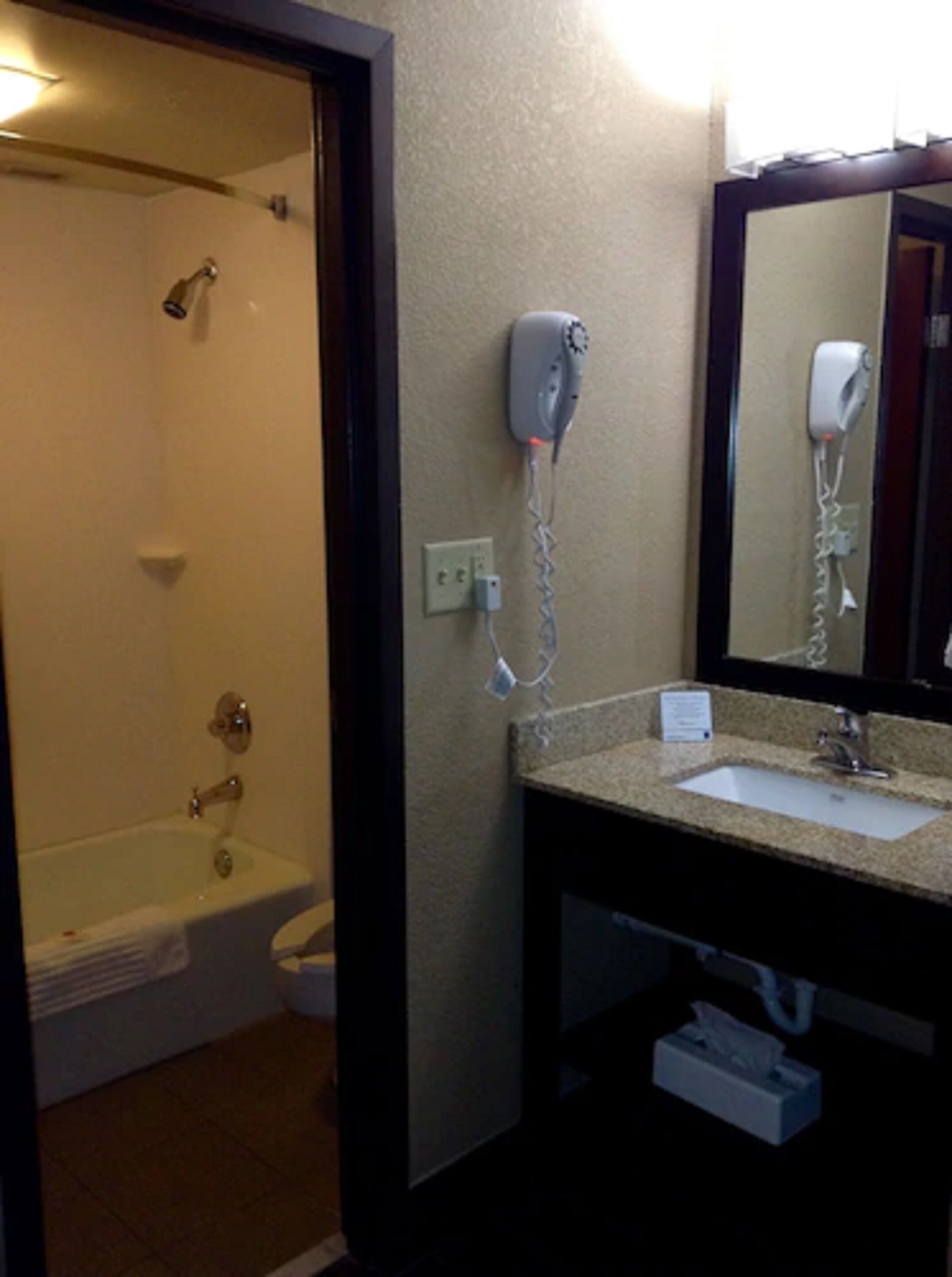 A bathroom with a bathtub, a sink, a mirror, and a hairdryer mounted on the wall.
