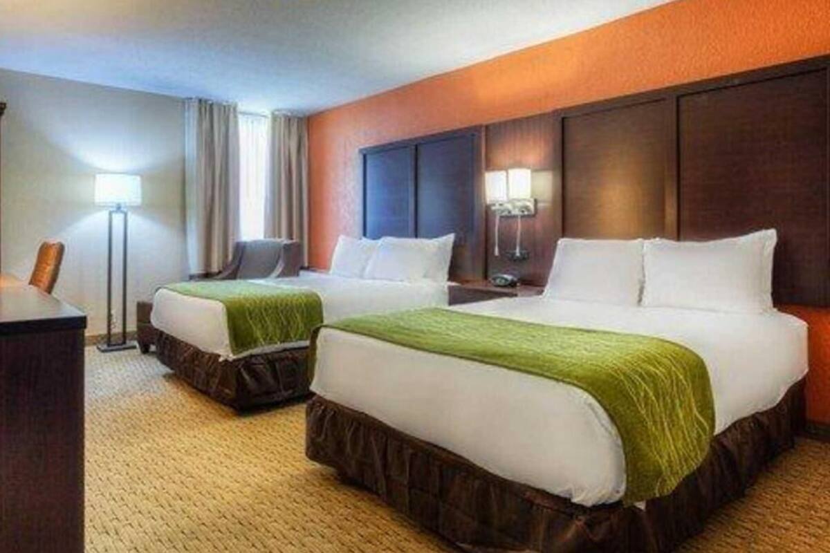 A hotel room with two beds, a desk, and a lamp.