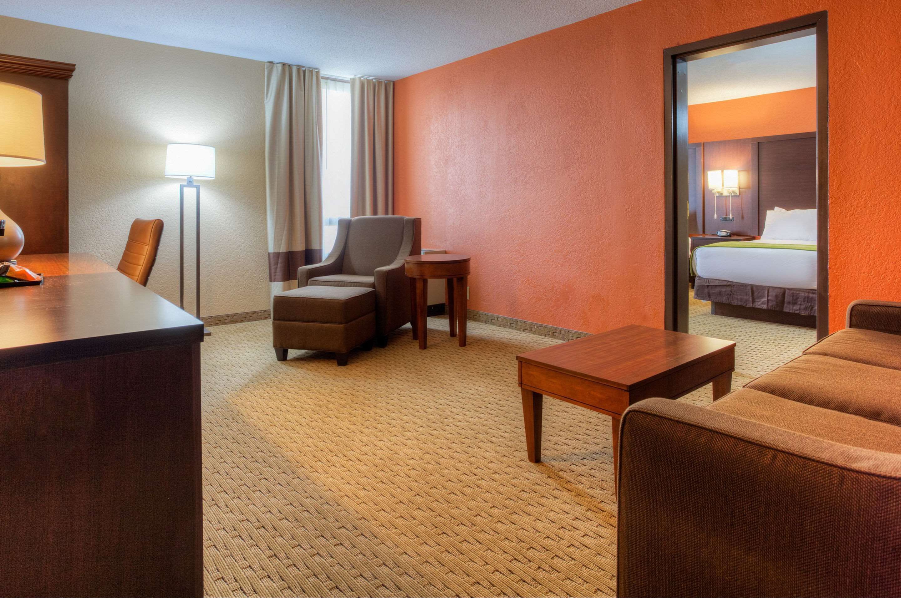 Une chambre d’hôtel avec un grand lit, un bureau, deux fauteuils, une petite table et une lampe sur pied.