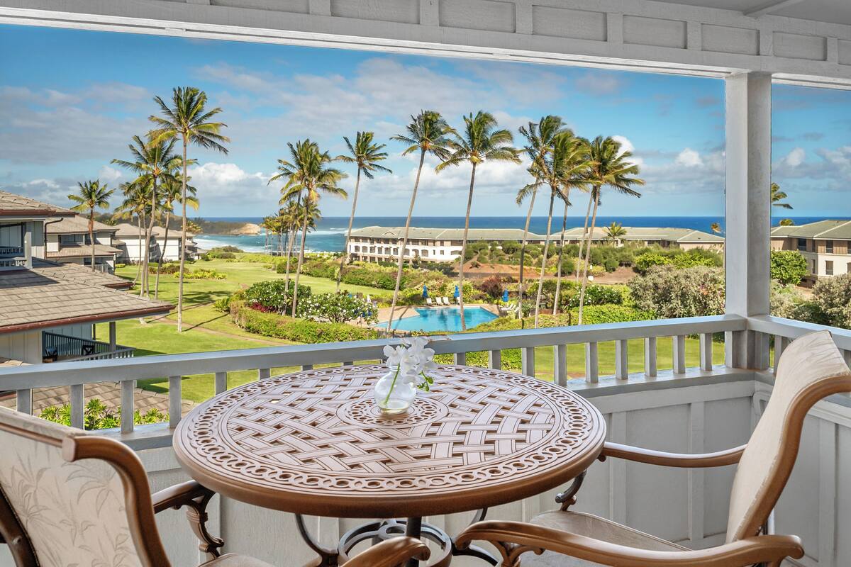 A balcony with a view of a pool, palm trees, and a building across the water.