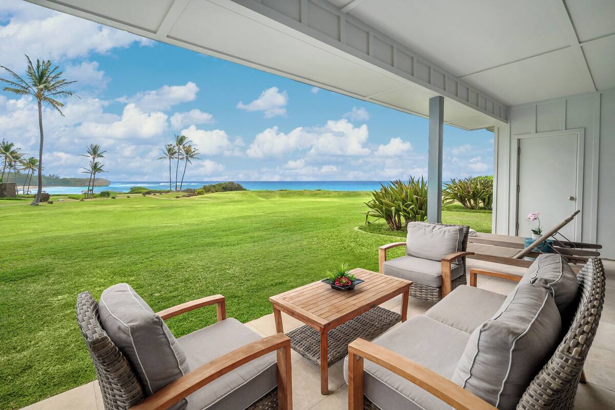 A covered outdoor seating area with a view of a golf course and ocean.