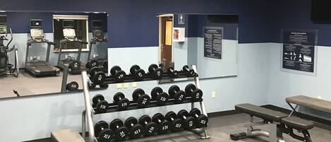 A gym with treadmills, weight benches, and a rack of dumbbells.