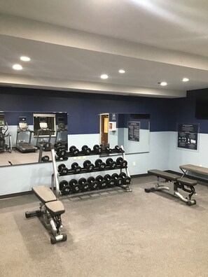 Ett gym med löpband, träningsbänkar och ett ställ med hantlar.