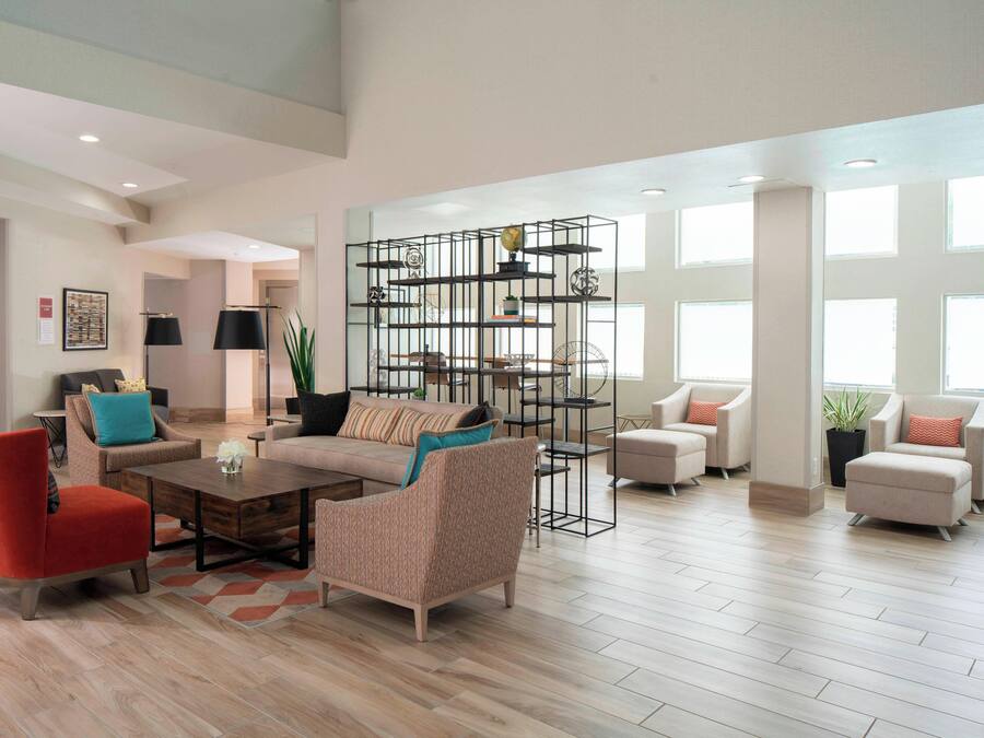 A spacious living room with a modern design, featuring a red armchair, a beige sofa, and a unique metal shelving unit.
