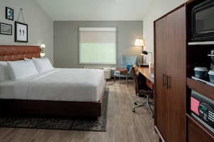Una habitación de hotel con una cama grande, un escritorio, una silla, un televisor y un mini bar.