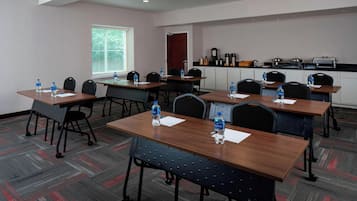 A conference room with tables, chairs, water bottles, a window with blinds, a kitchenette, and a door.