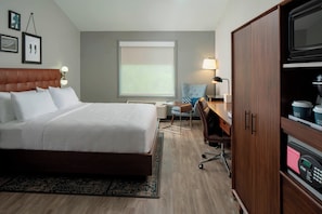 Habitación de hotel con cama, escritorio, silla, sofá, cafetera y televisión.
