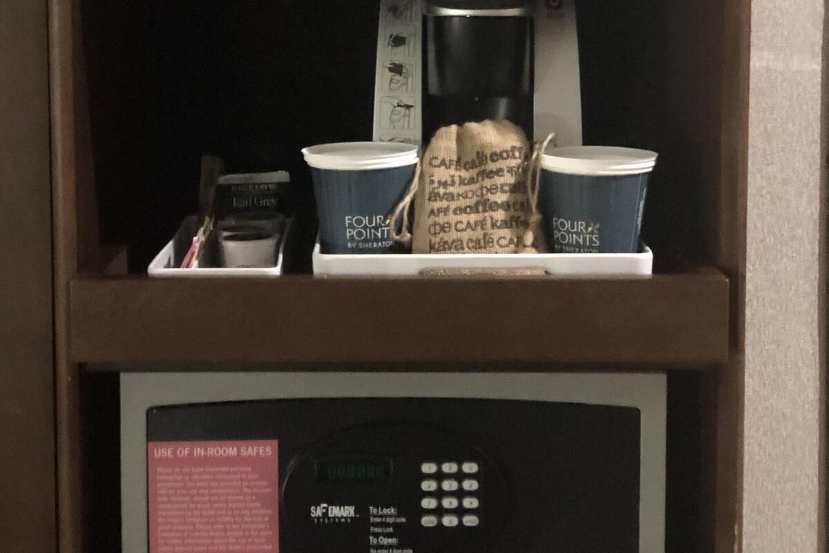 A microwave above a coffee maker with cups and a coffee bag.
