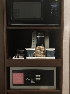 Un four à micro-ondes au-dessus d’une machine à café, avec des tasses et un paquet de café.