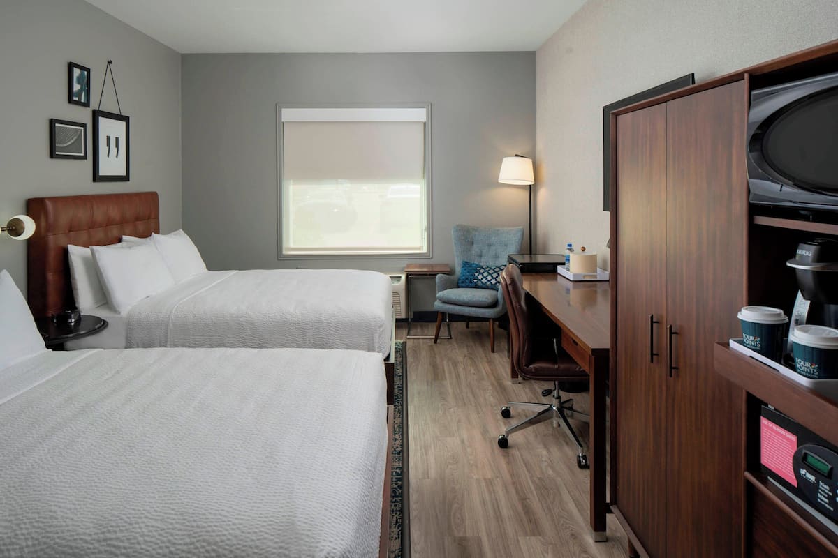 A hotel room with two beds, a desk with a lamp, a chair, a wardrobe, and a window with a view.