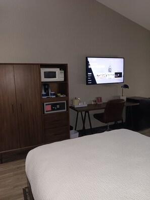 Une chambre d’hôtel équipée d’un lit, d’un bureau, d’une chaise, d’une télévision, d’une armoire et d’un four à micro-ondes.