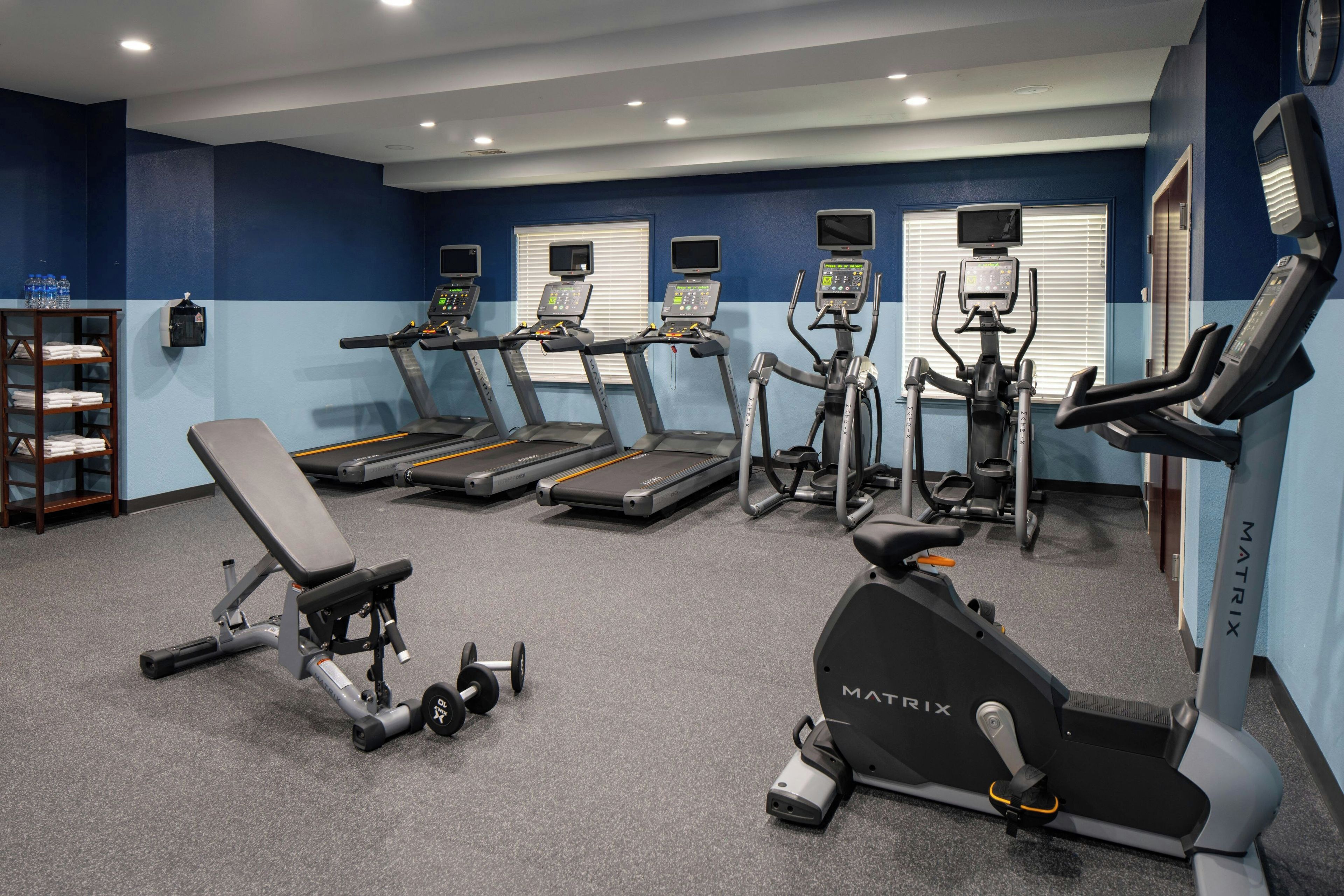 A gym with treadmills, elliptical machines, and a bench.