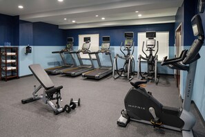 Un gimnasio con cintas de correr, elípticas y un banco.