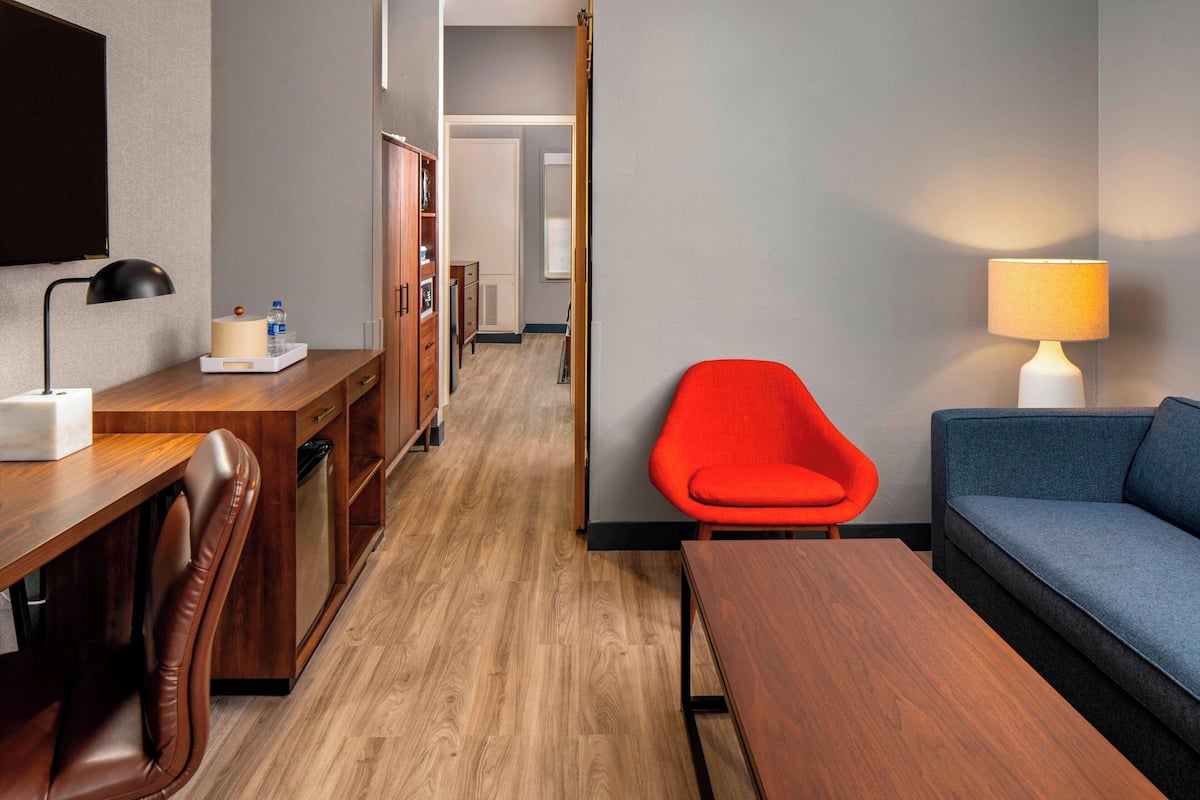 A hotel room with a wooden desk, a red chair, a blue sofa, and a lamp.