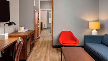 A hotel room with a wooden desk, a red chair, a blue sofa, and a lamp.