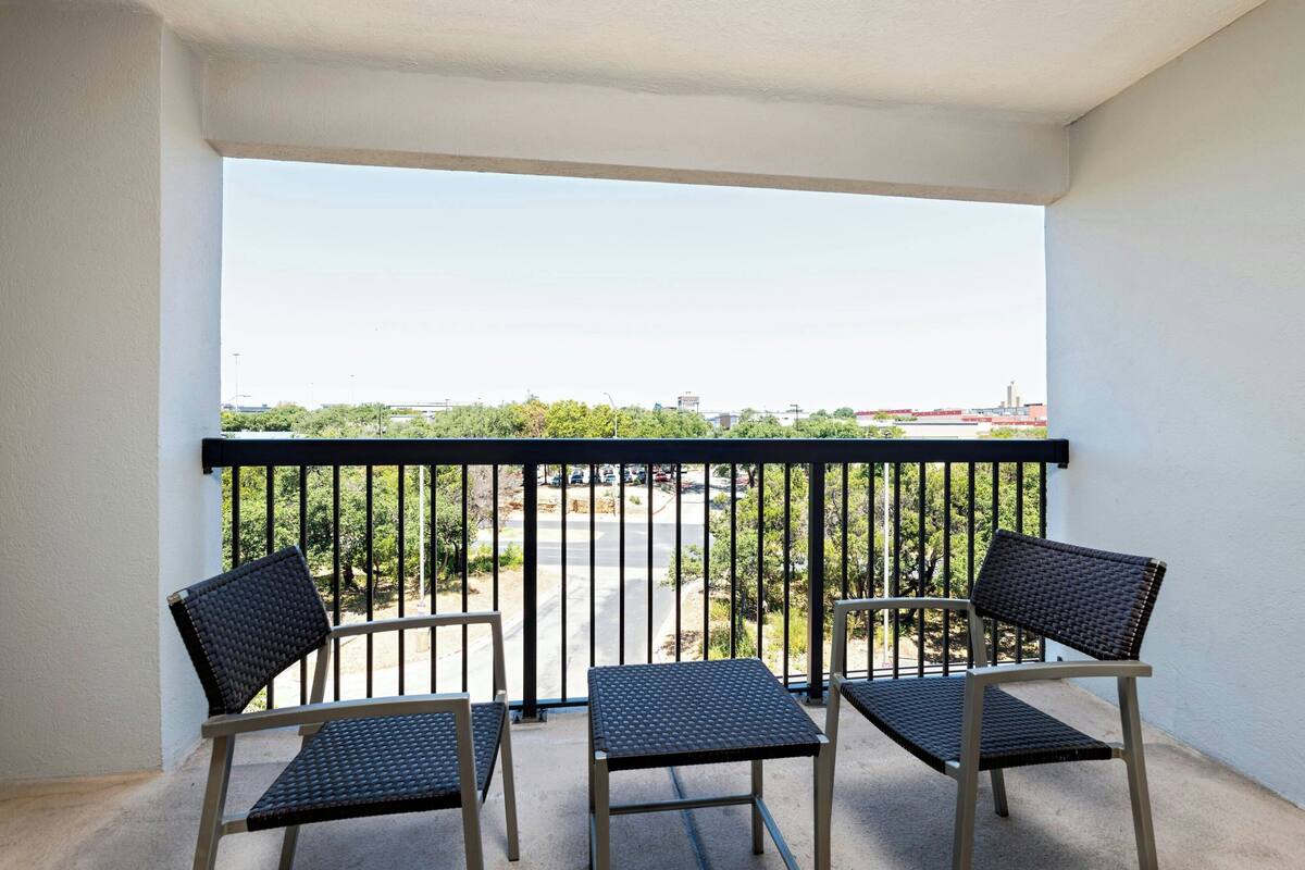 A balcony with two chairs and a table, overlooking a parking area and greenery.