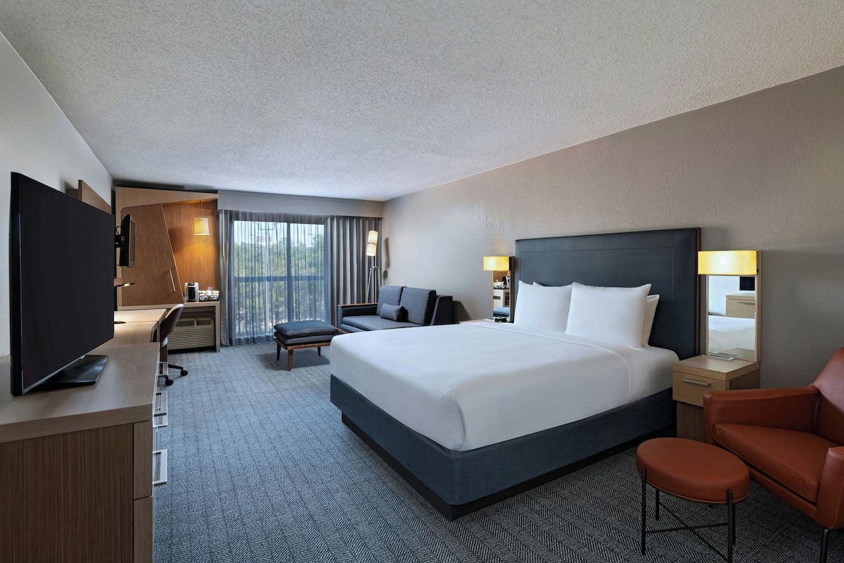 A hotel room with a large bed, a desk with a computer, a TV, and a seating area with a sofa and armchairs.