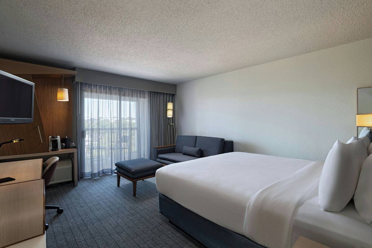 A hotel room with a large bed, a desk with a chair, a television, and a window with curtains.