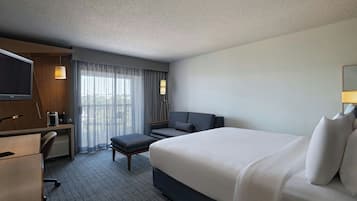 A hotel room with a large bed, a desk with a chair, a television, and a window with curtains.