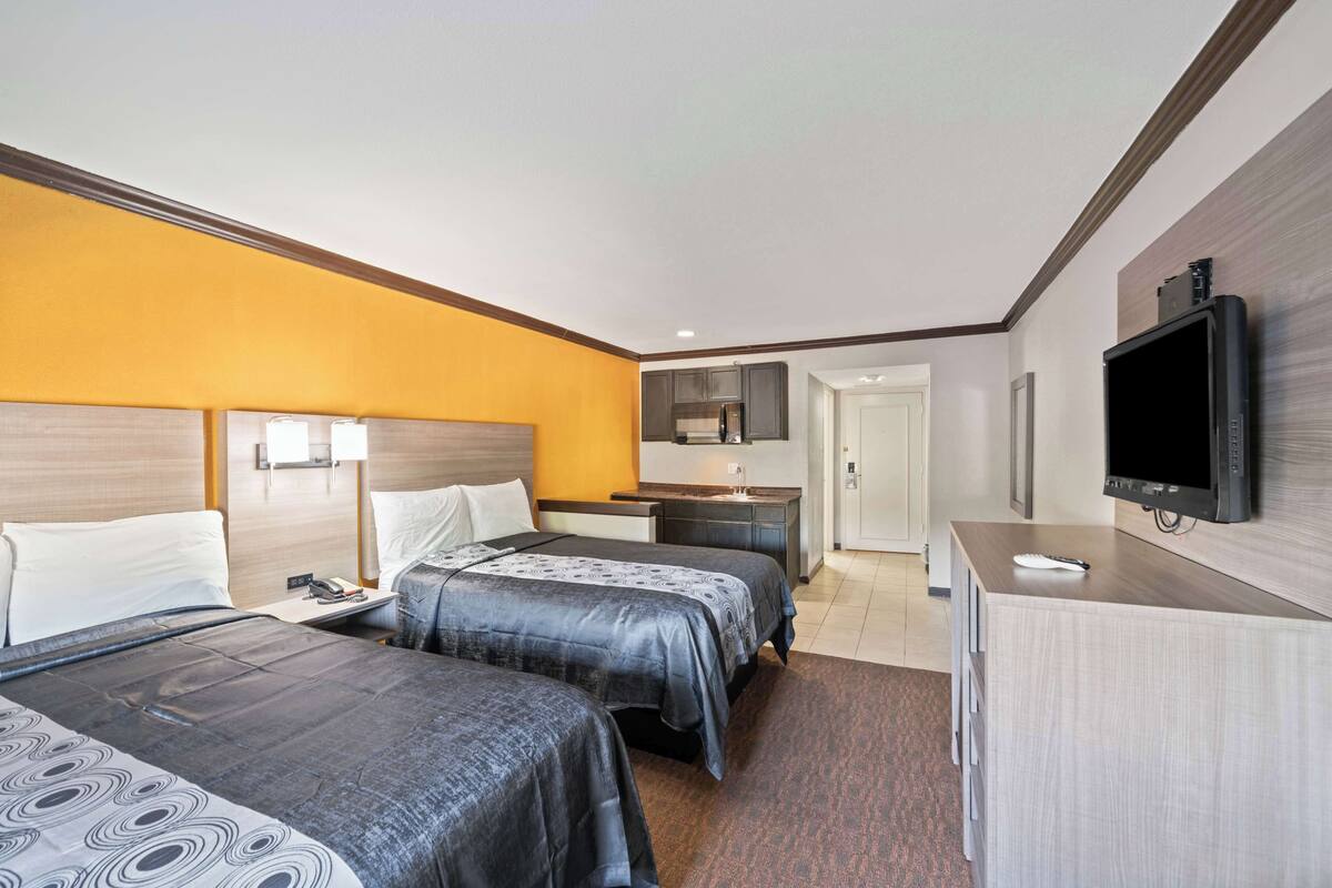 A hotel room with two beds, a desk, a television, and a bathroom visible through an open door.