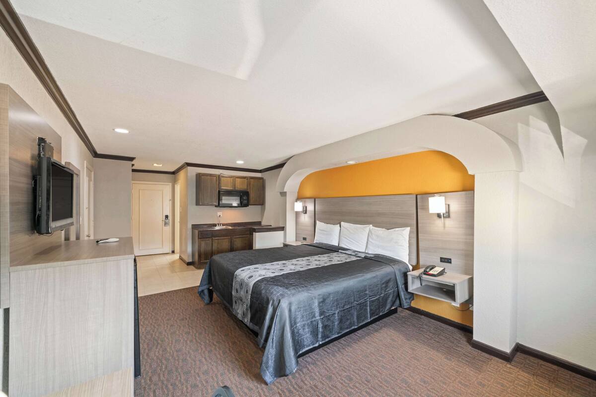 A hotel room with a bed, bedside table, lamp, and a TV mounted on the wall.