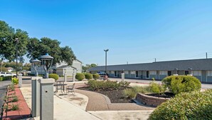 A motel with a landscaped garden, outdoor seating, and a parking lot.
