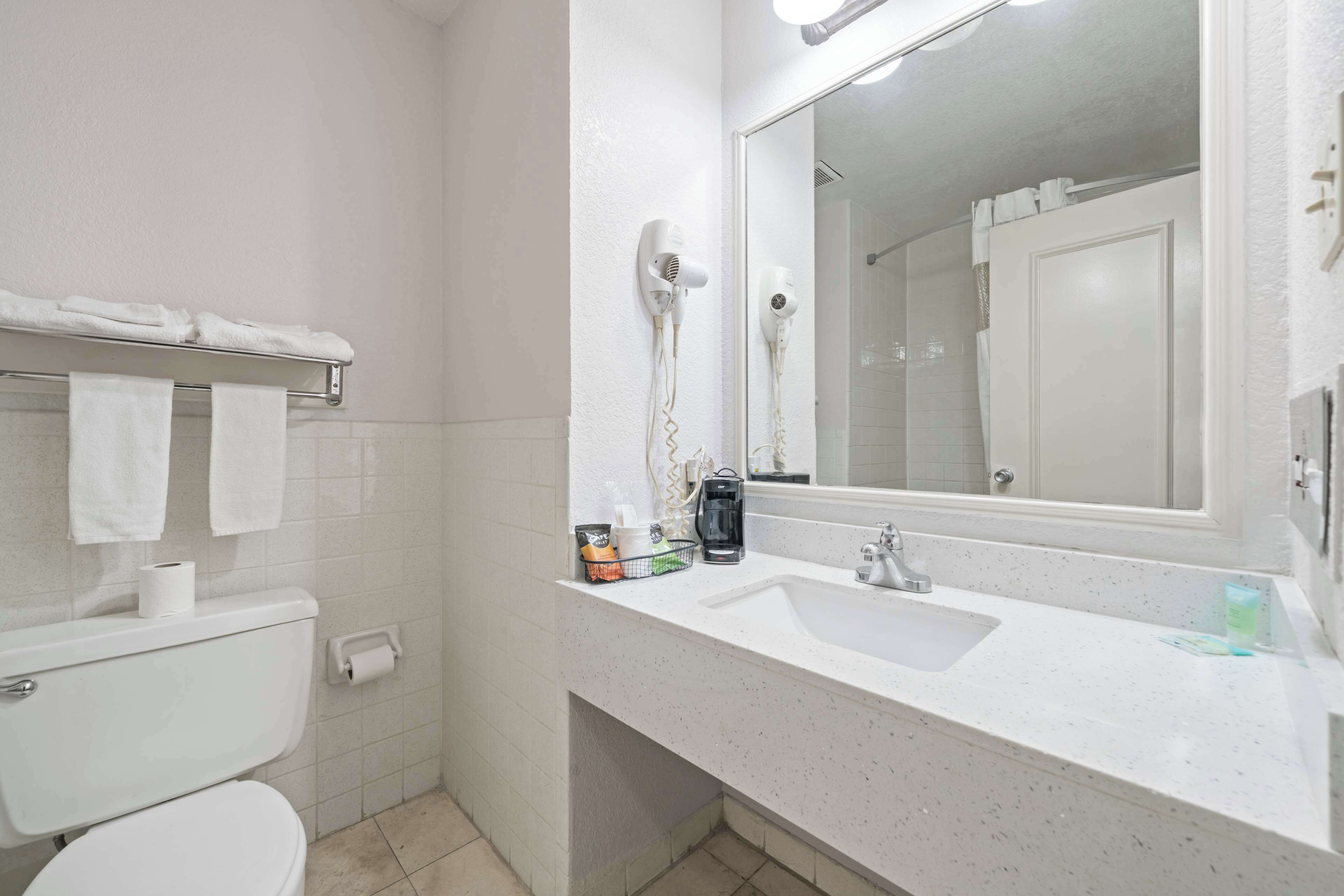A bathroom with a toilet, sink, towel rack, and two hair dryers mounted on the wall.