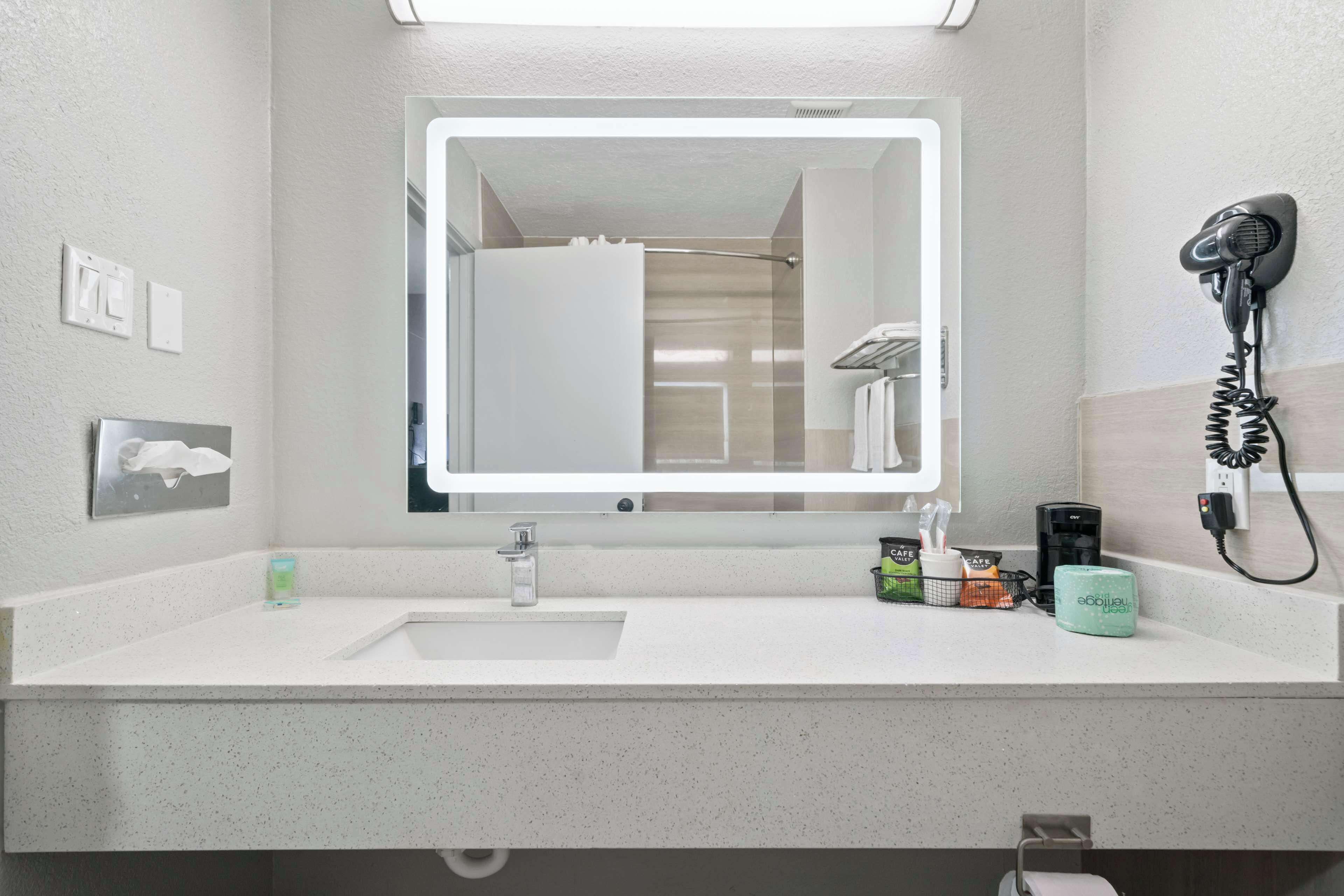 A modern bathroom with a large mirror, a sink, a hairdryer, and a coffee machine.