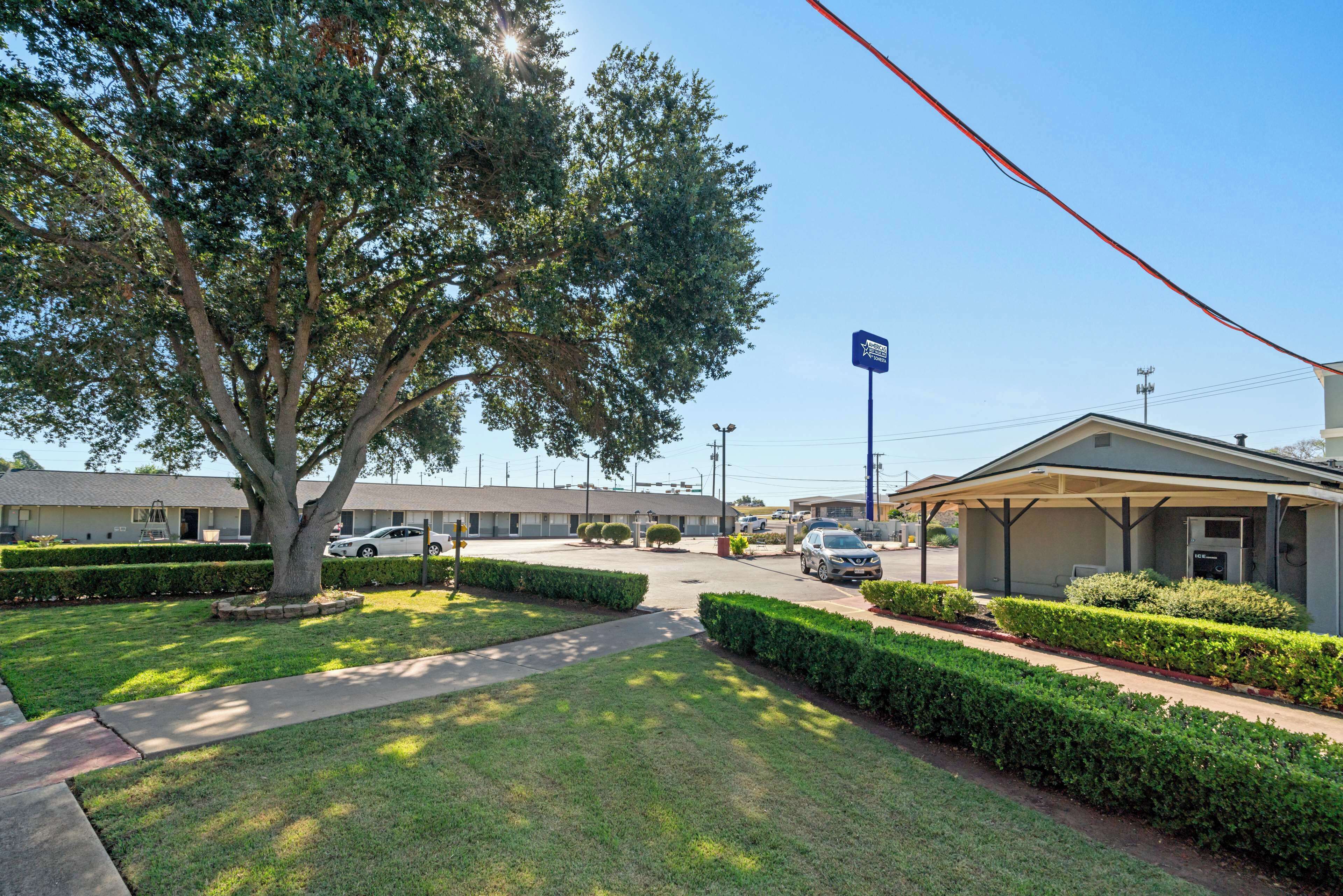 A motel with a covered parking area, a large tree, and a clear sky.