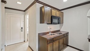 A compact kitchen with wooden cabinets, a microwave, and a double sink. - Americas Best Value Inn & Suites Brenham (Brenham)
