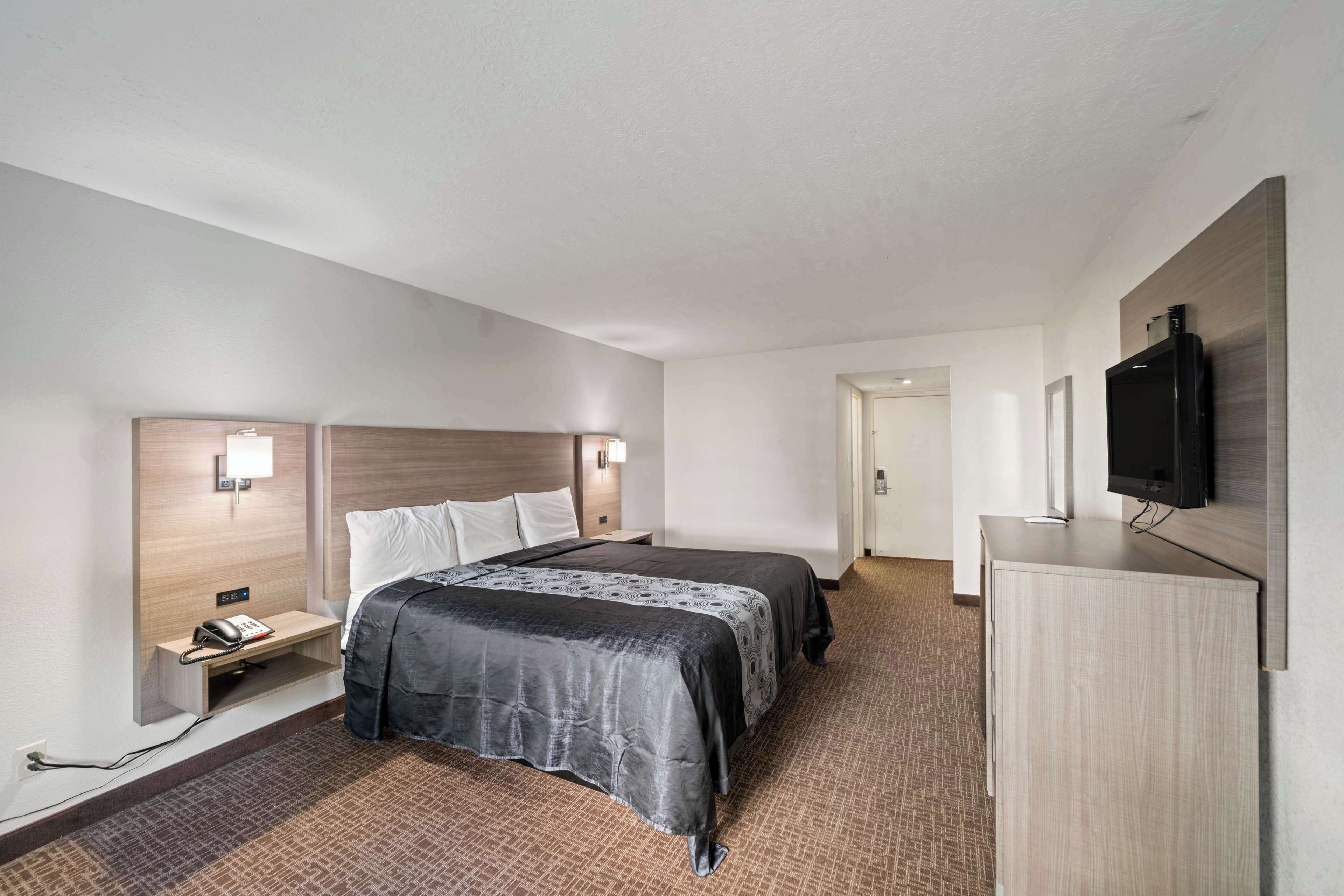 Een hotelkamer met een bed, nachtkastjes, een televisie en een vloerbedekking.