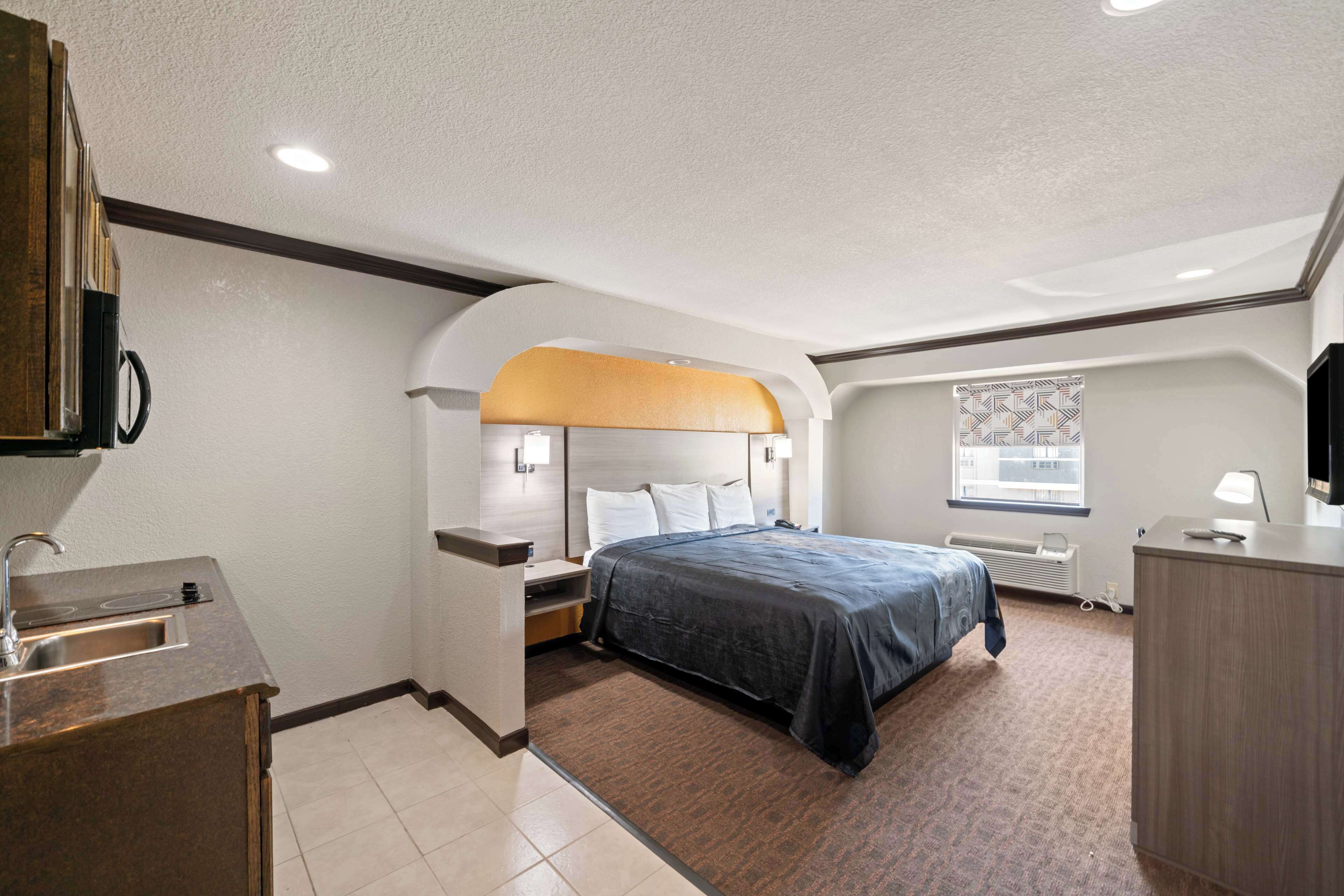 A hotel room with a bed, a desk, a sink, and a window.