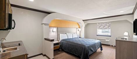 A hotel room with a bed, a desk, a sink, and a window.