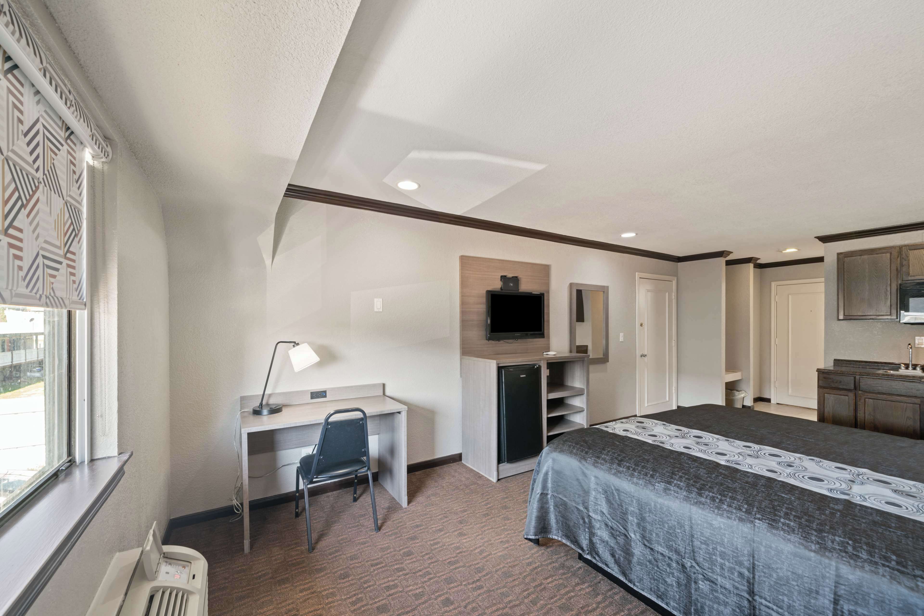 A hotel room with a bed, desk, chair, television, and a small refrigerator.