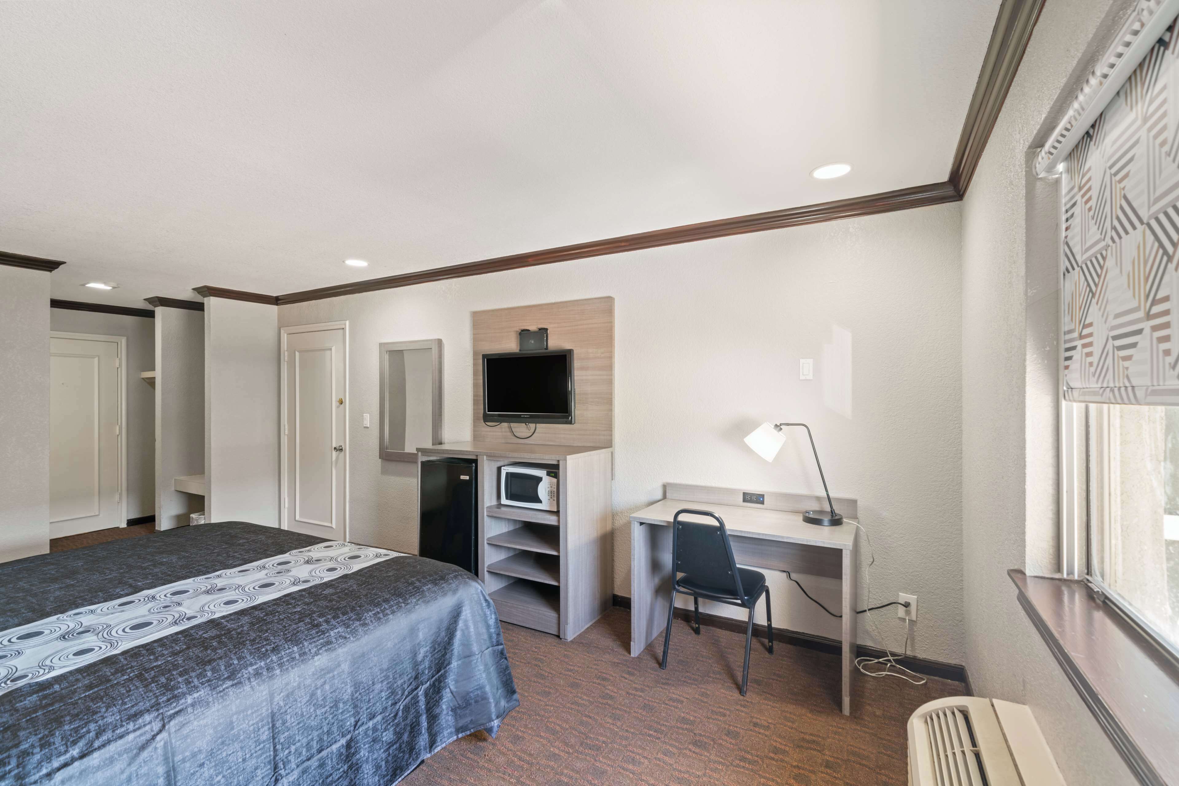 Habitación de hotel con cama, escritorio con silla, televisor, microondas y ventana con vistas.