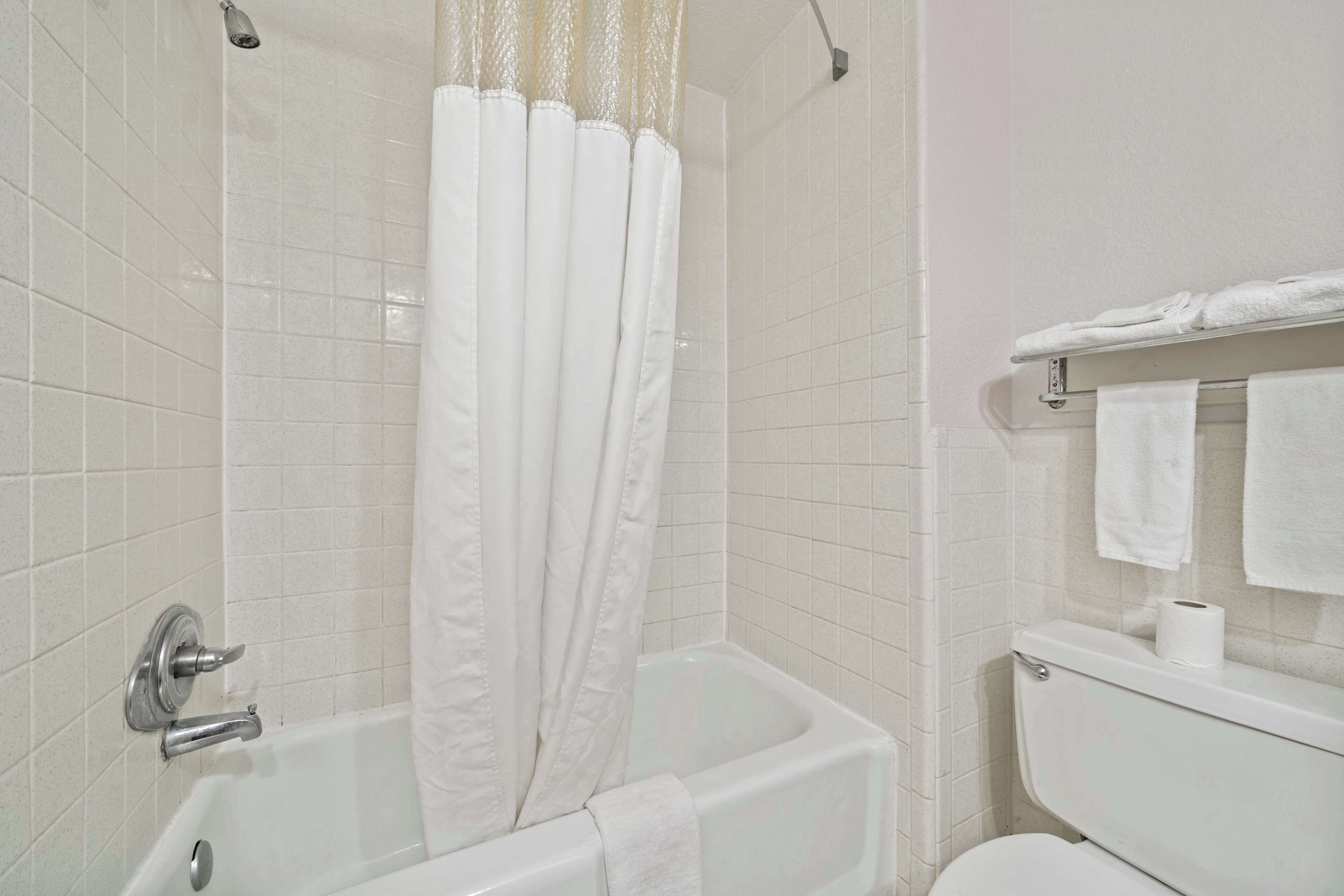 Un baño con una bañera blanca, una cortina de ducha, un inodoro y un perchero para toallas.