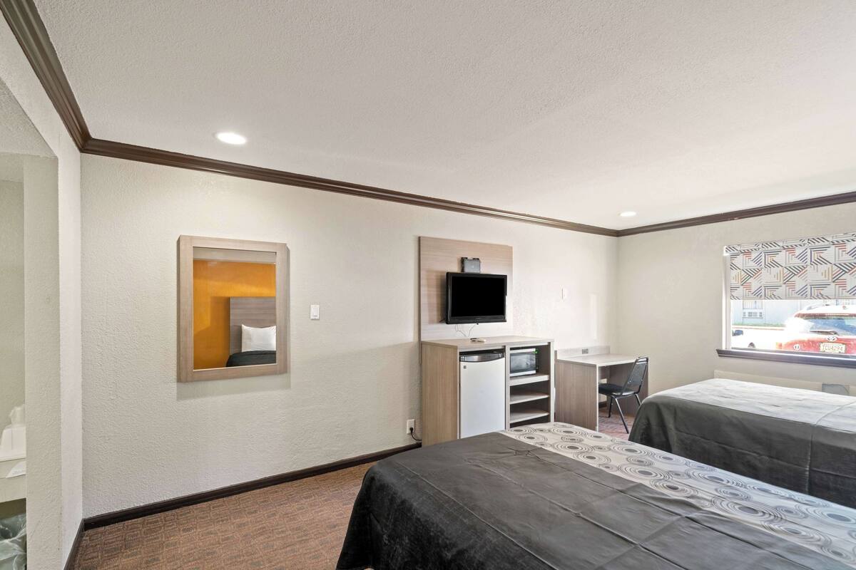 A hotel room with two beds, a desk, a television, and a window with a view of a red car.