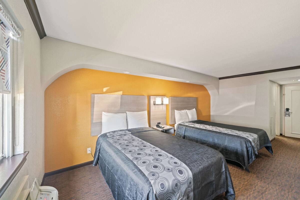 A hotel room with two beds, a nightstand, and a window with curtains.