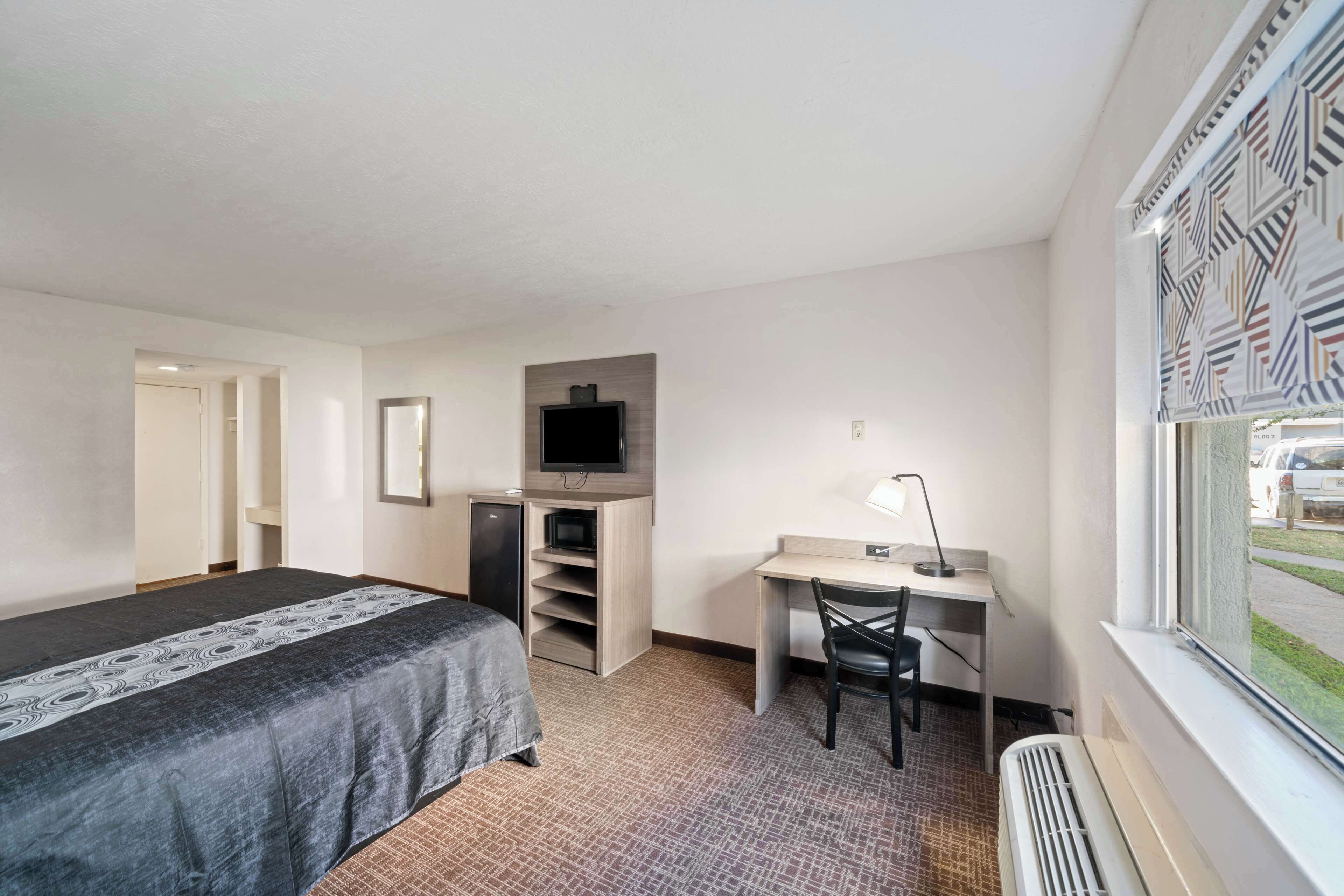 A hotel room with a bed, desk, chair, TV, and a window with a view.