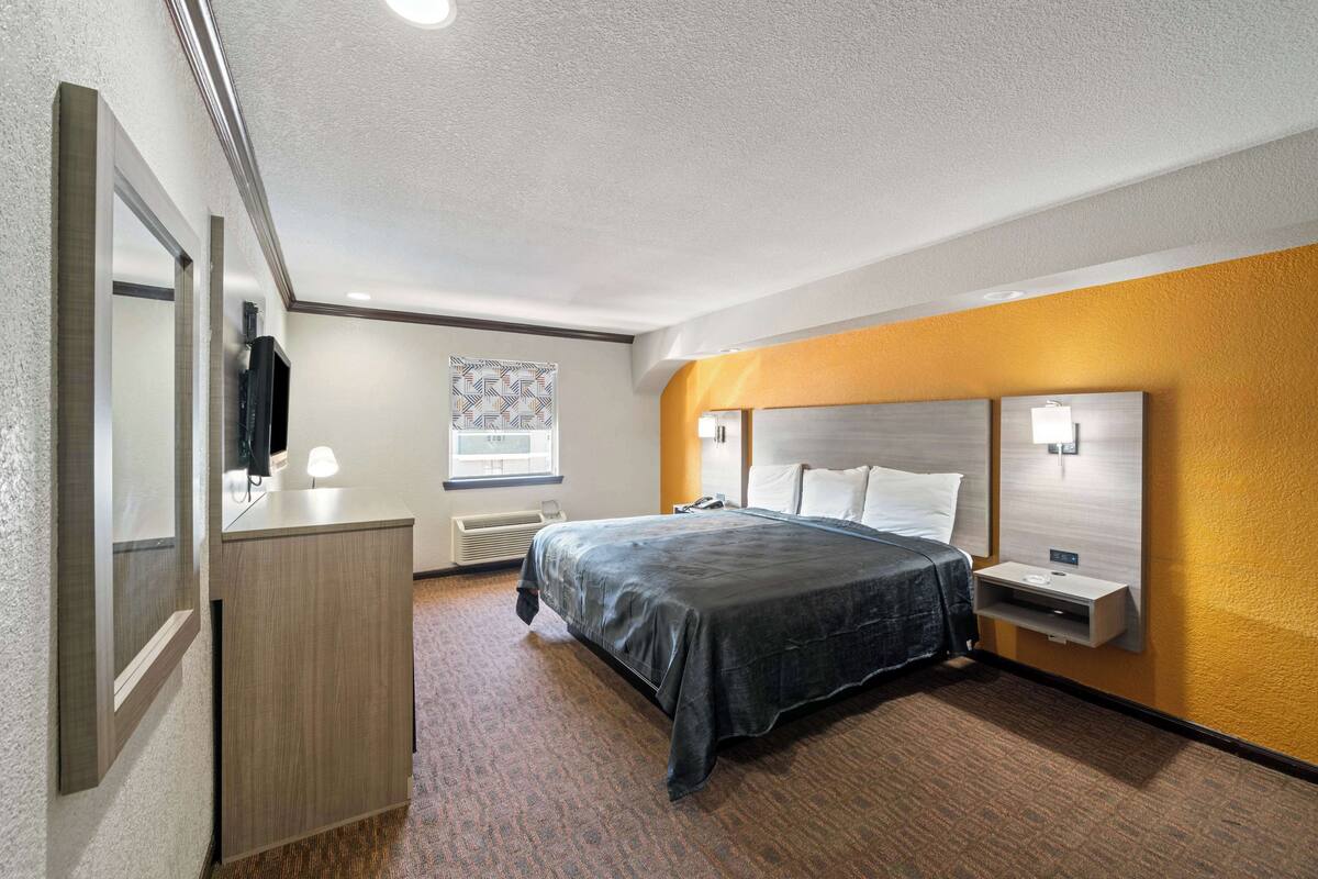 A hotel room with a bed, bedside table, lamp, and a mirror.