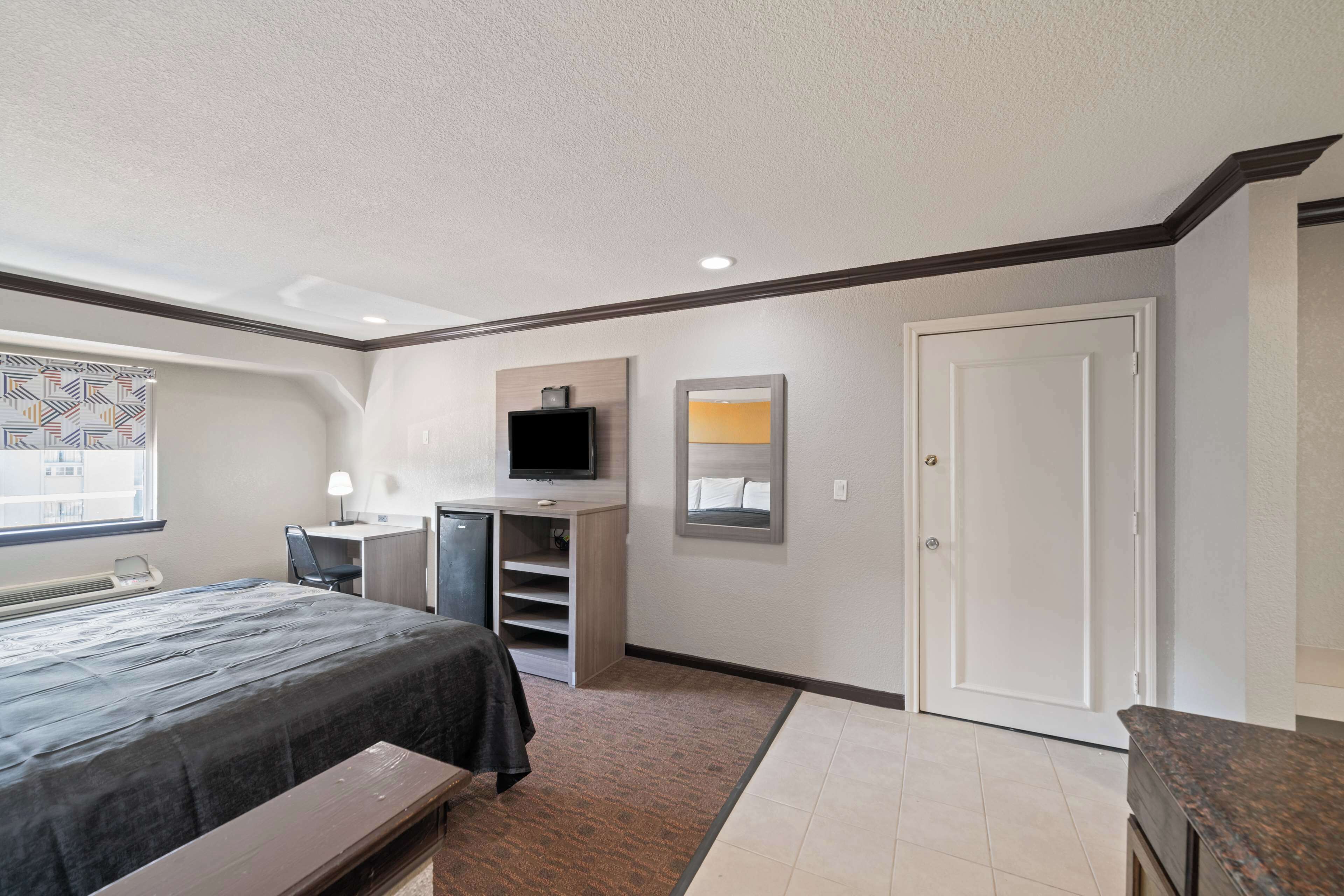 A hotel room with a bed, desk, chair, TV, and a door.