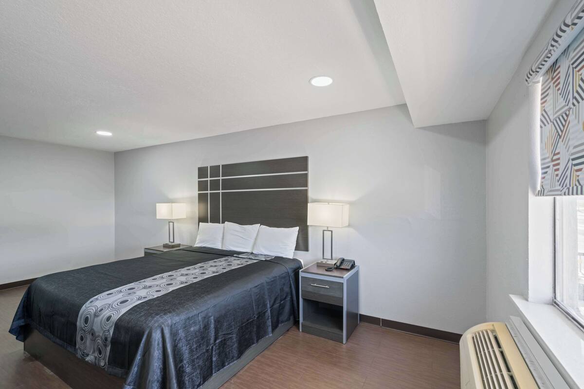 A hotel room with a bed, bedside tables, lamps, and a window with a patterned curtain.