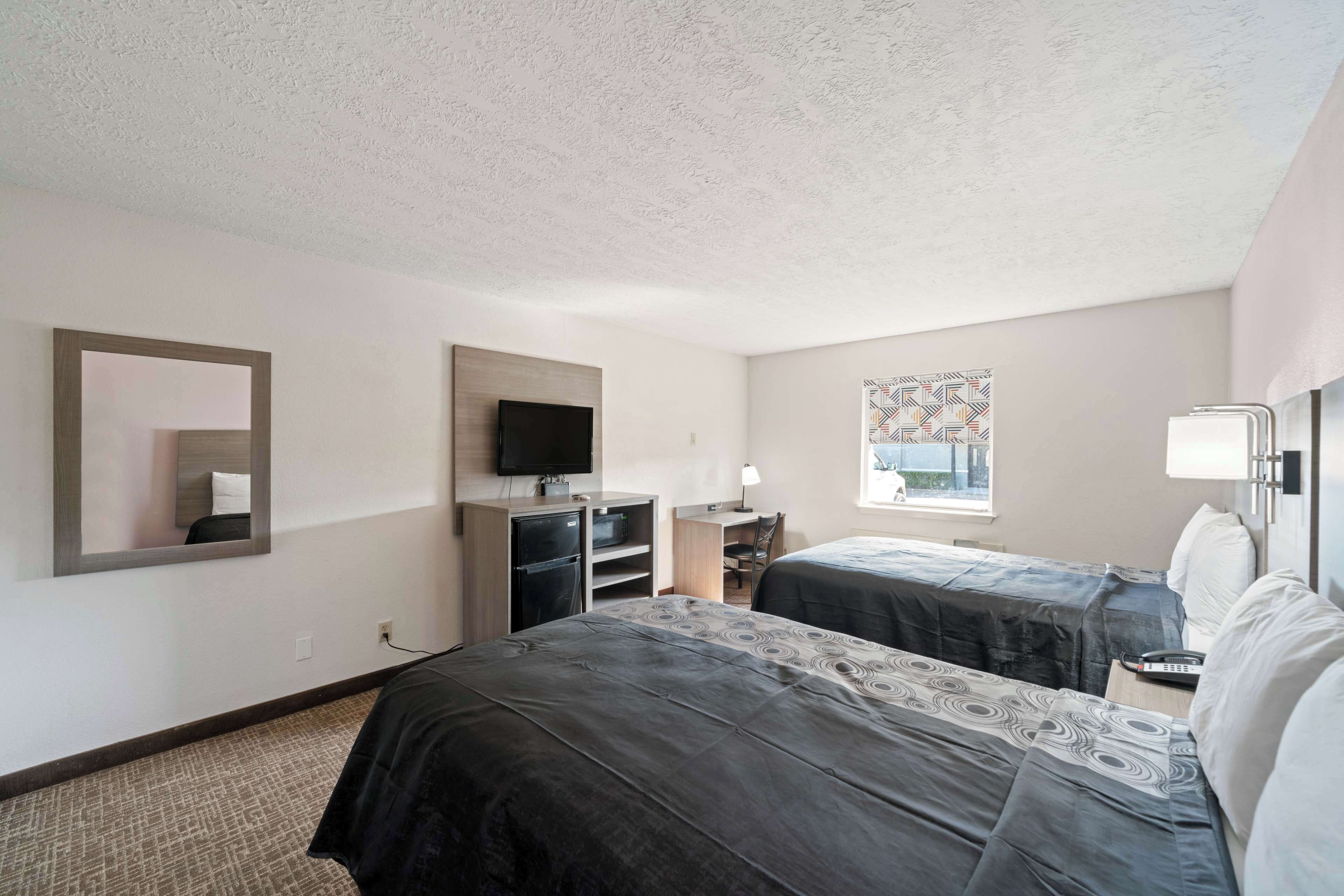 A hotel room with two beds, a TV, a desk, and a window with a patterned curtain.