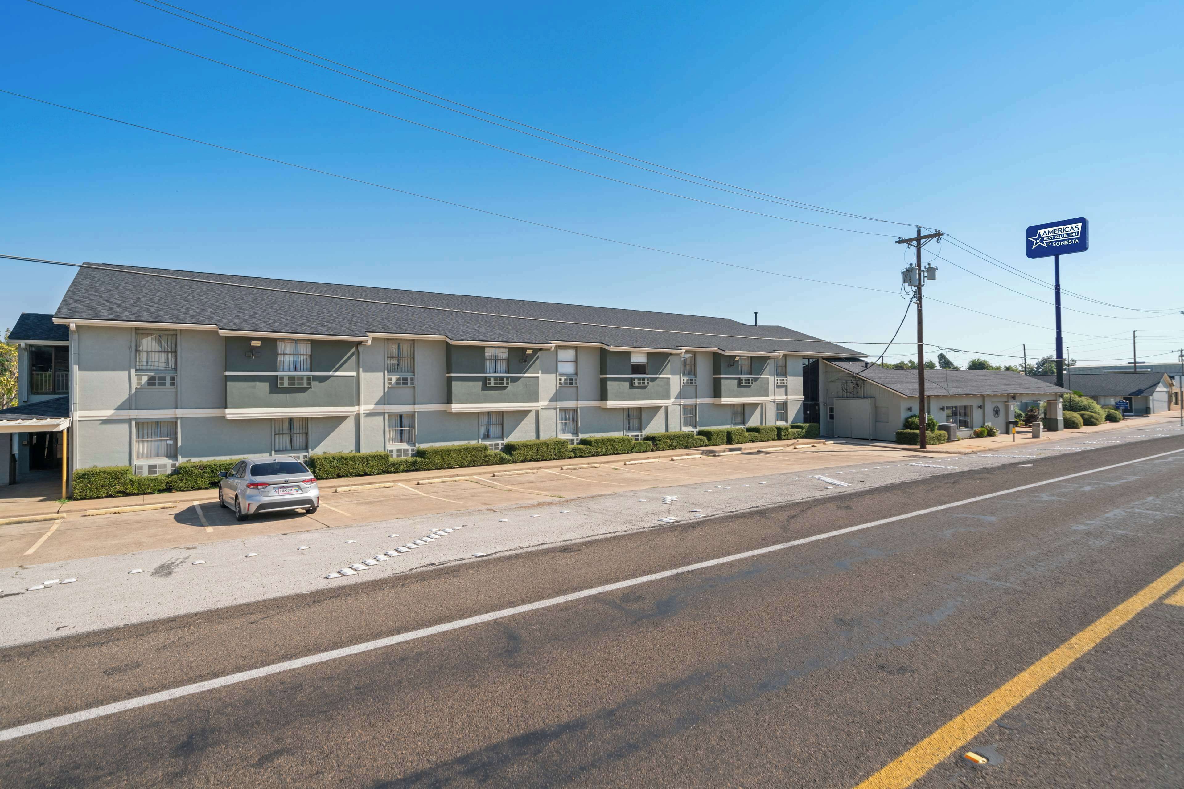 A motel with a row of rooms, a parking lot, and a clear sky.