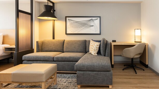 A modern living room with a sectional sofa, a small table, a desk with a chair, and a framed abstract artwork on the wall.