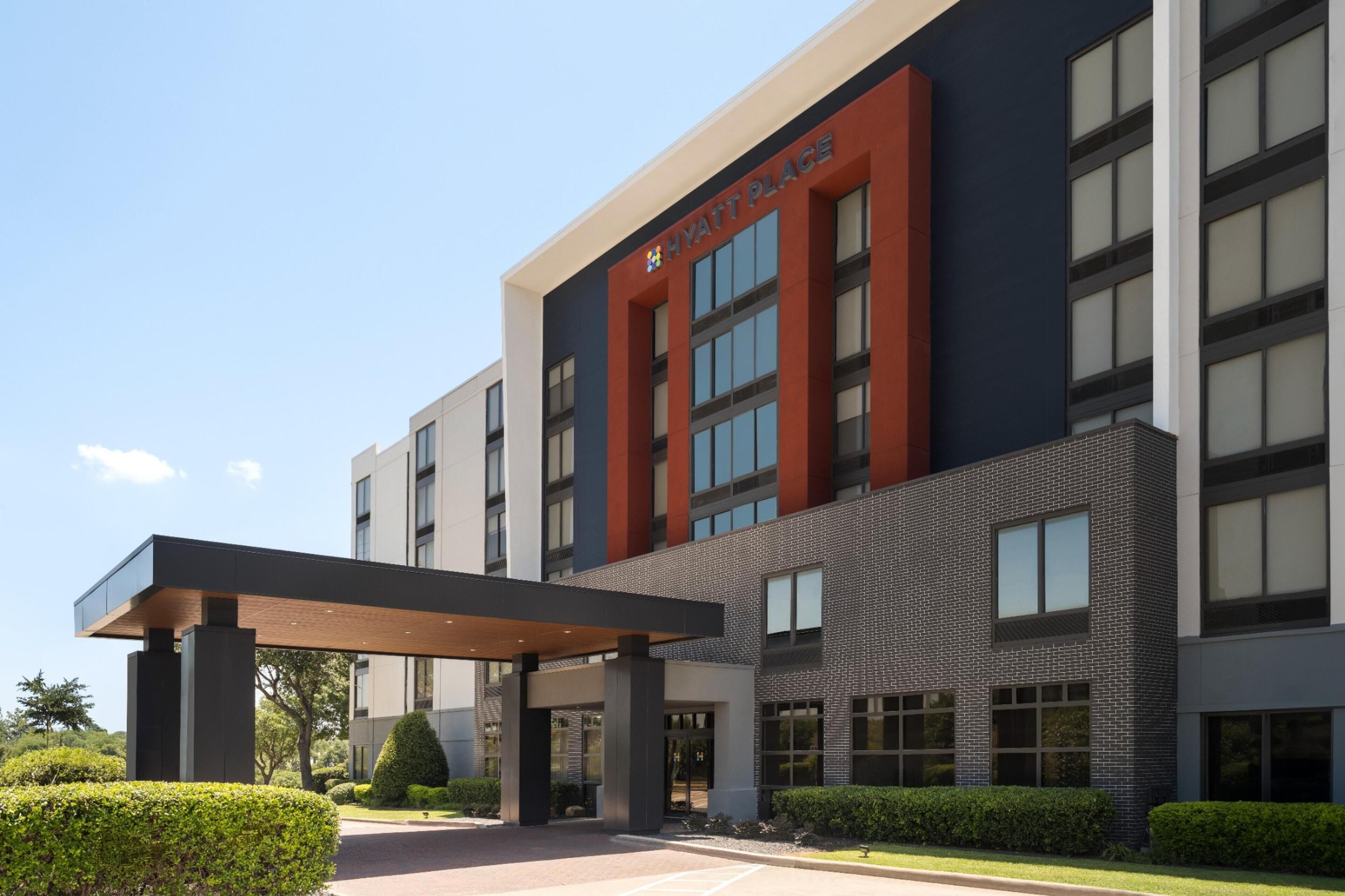 A modern hotel building with a prominent entrance, large windows, and a covered walkway.